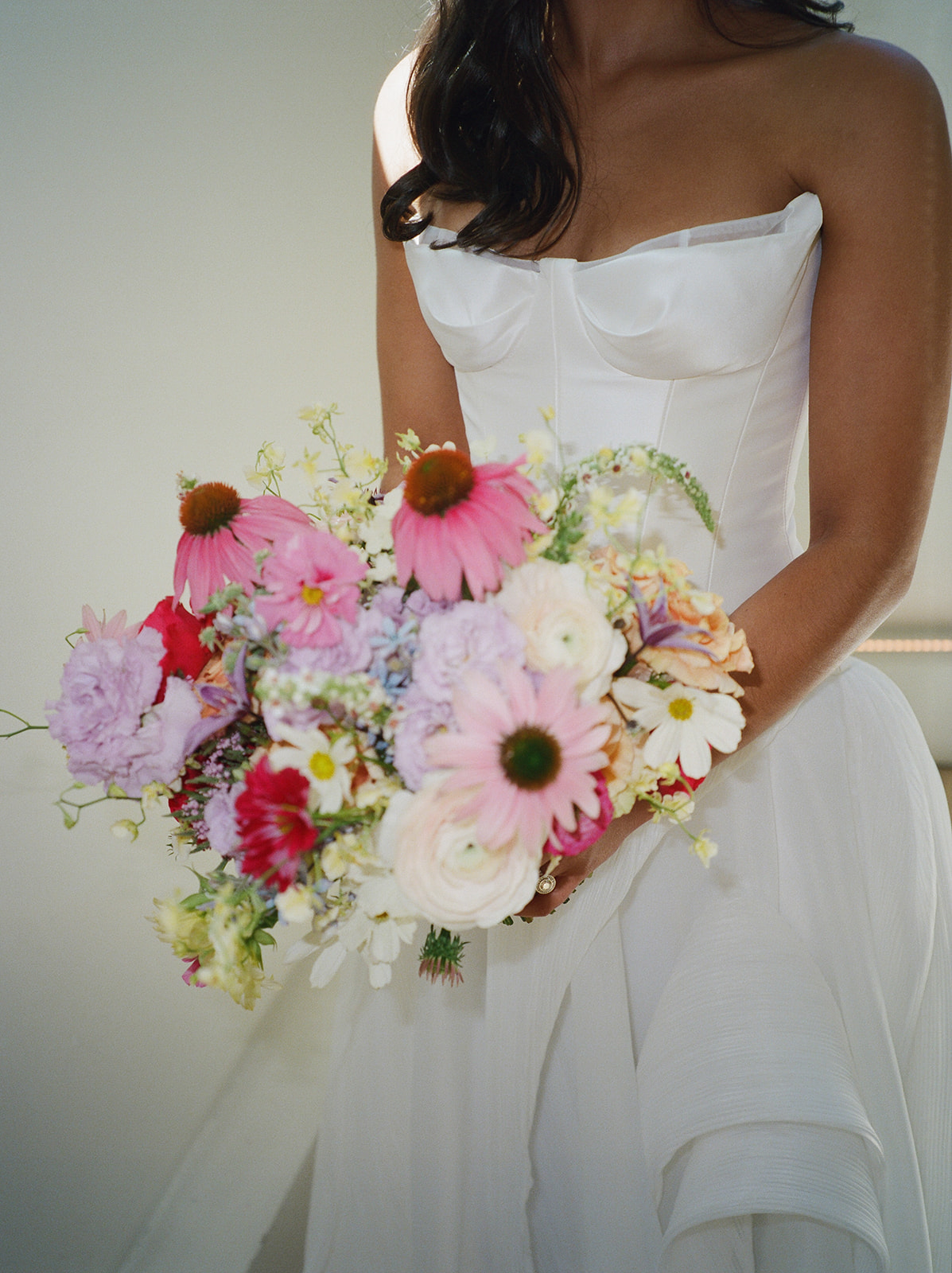 A bride holds a bouquet of bright summer flowers