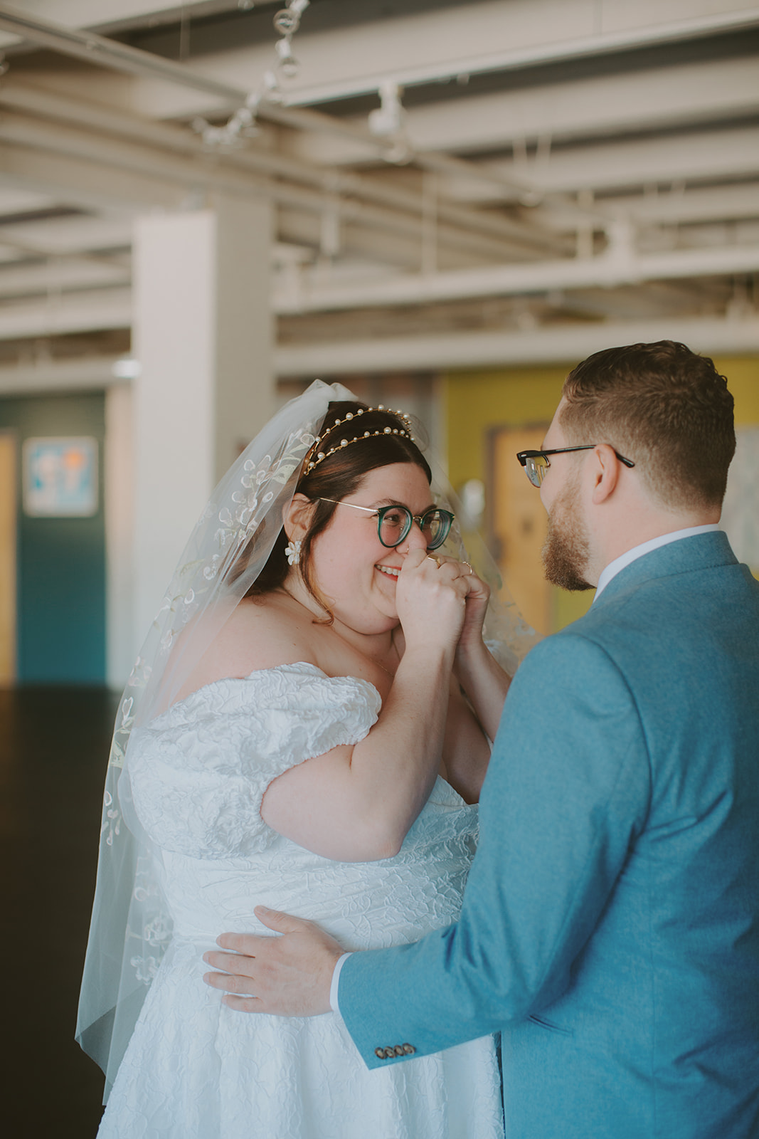 A bride and groom smile at each other in an art gallery